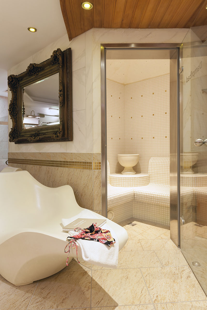 Modern wellness area with a lounger and steam bath in the background, surrounded by elegant details.