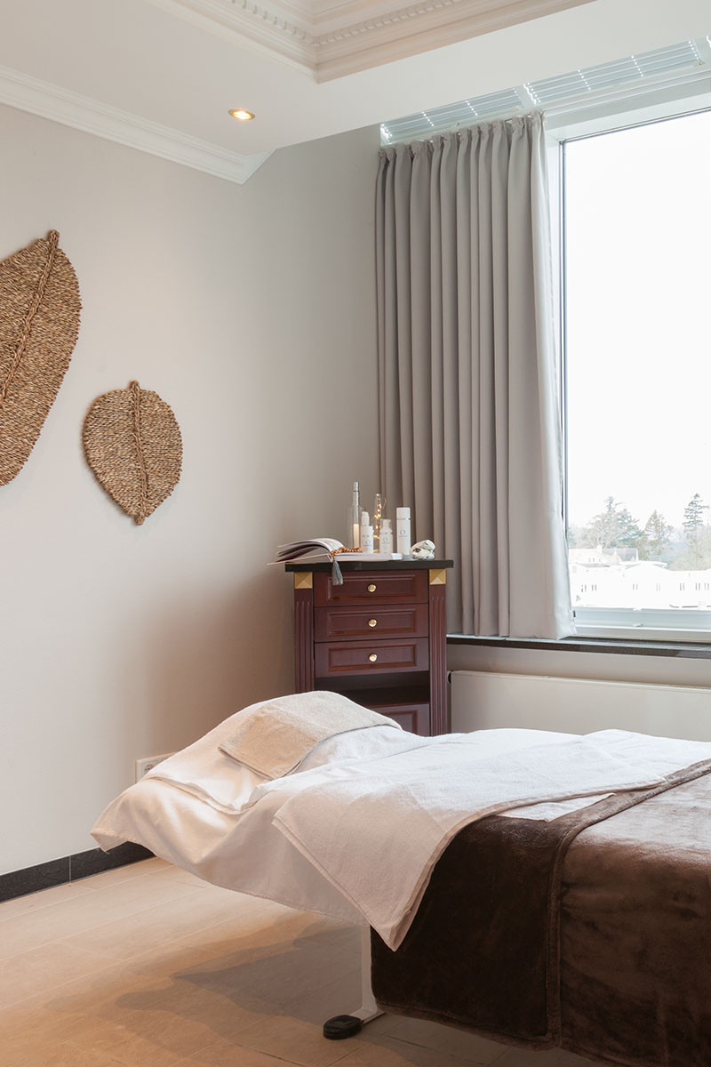 Bright treatment room with a massage table and simple wall decorations next to a window.