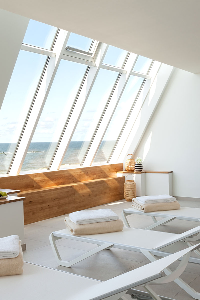 Modern relaxation room with large windows, white loungers and a direct view of the sea.