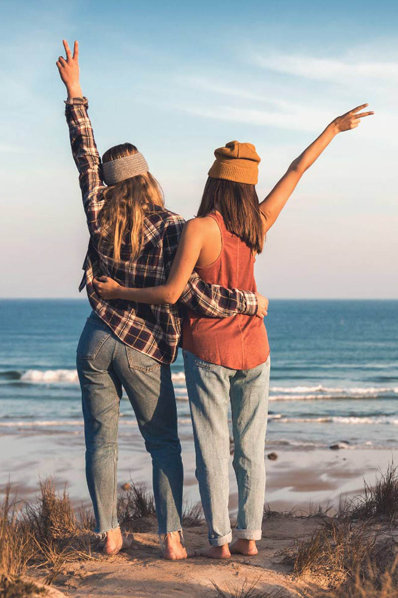 Rückansicht von zwei Frauen, die sich umarmen und den Ausblick auf das Meer genießen.