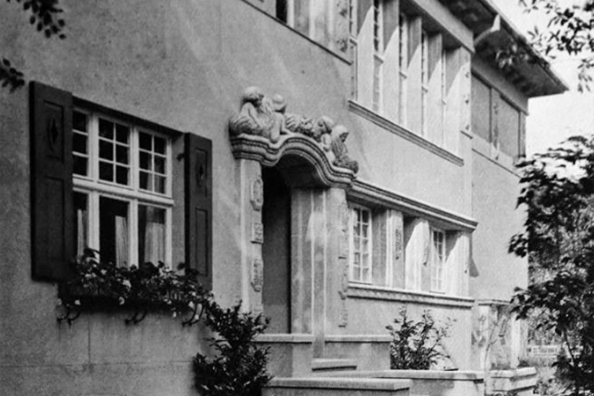 Schwarzweiß-Aufnahme eines historischen Gebäudes mit verziertem Eingang und großen Fenstern.