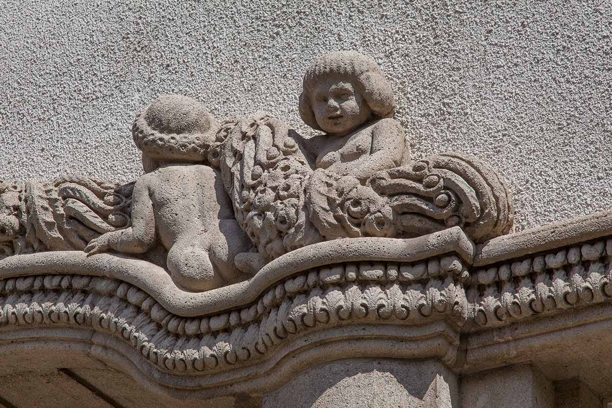 Nahaufnahme von zwei steinernen Figuren, die aufwendig in eine Fassade eingearbeitet sind.