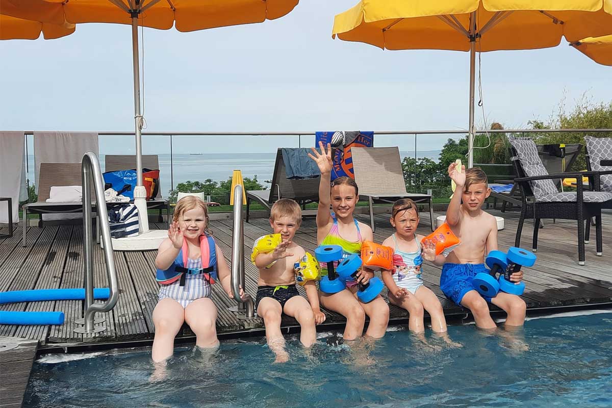 Five children sit at the edge of the pool at Kaiserhof Heringsdorf with water wings and swimming boards, ready for swimming lessons.