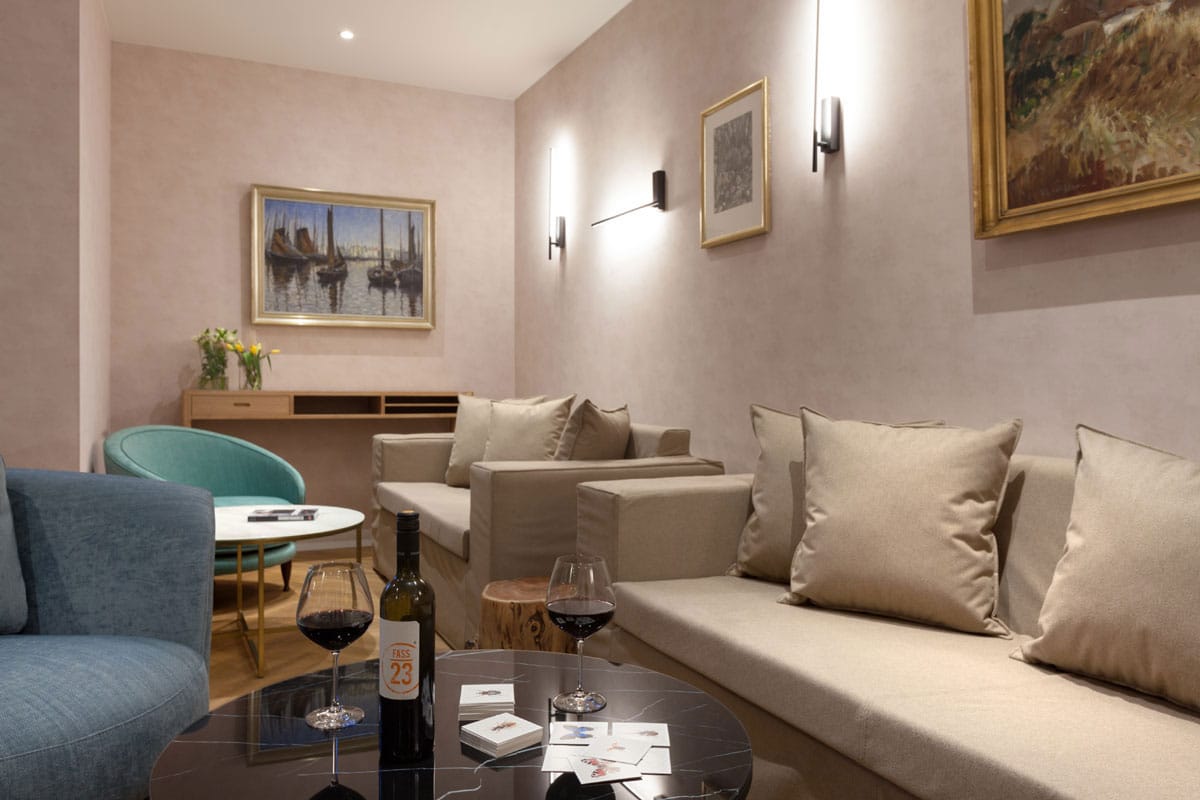 Lounge Wohnzimmer im Vju Hotel auf Rügen mit gemütlicher Couch, Wein und Kunst an den Wänden für entspannte Abende.