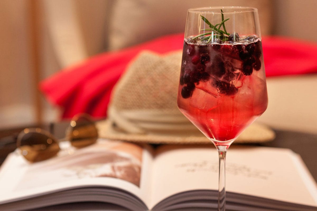 Fruchtiger Cocktail im Weinglas mit roten Beeren und Rosmarin in entspannter Lounge-Atmosphäre im Wohnzimmer auf Rügen.