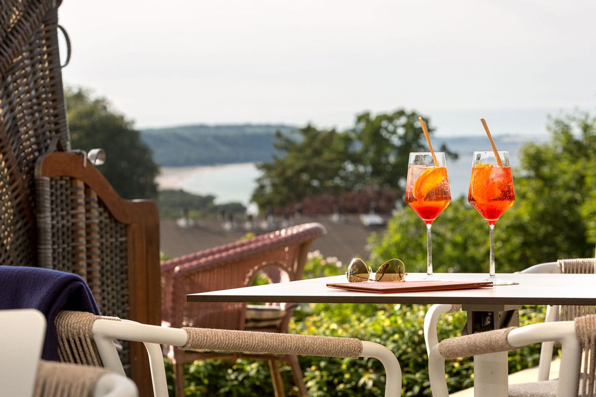 Gemütliche Terrasse mit Gläsern Aperitif und einem weiten Blick auf die Ostseeküste, eingerahmt von Natur im Vju Hotel.