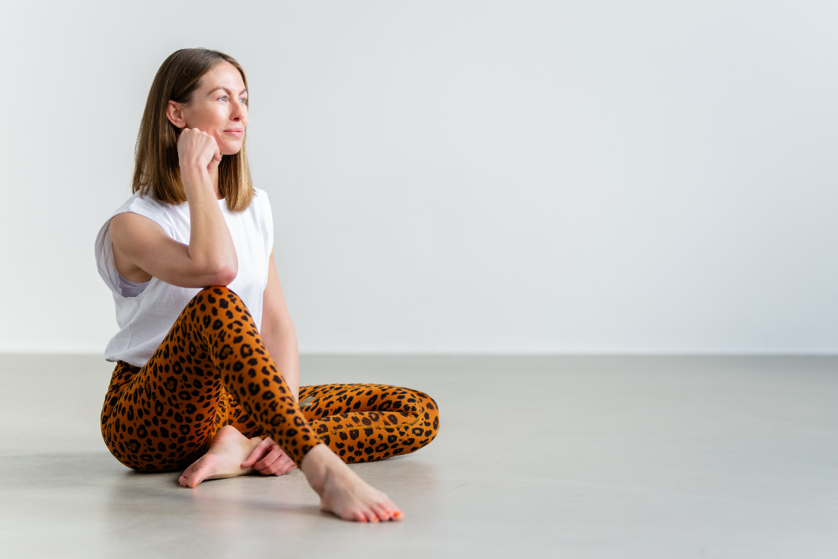 Eine junge Frau in Yogakleidung sitzt auf dem Boden ihres Studios.