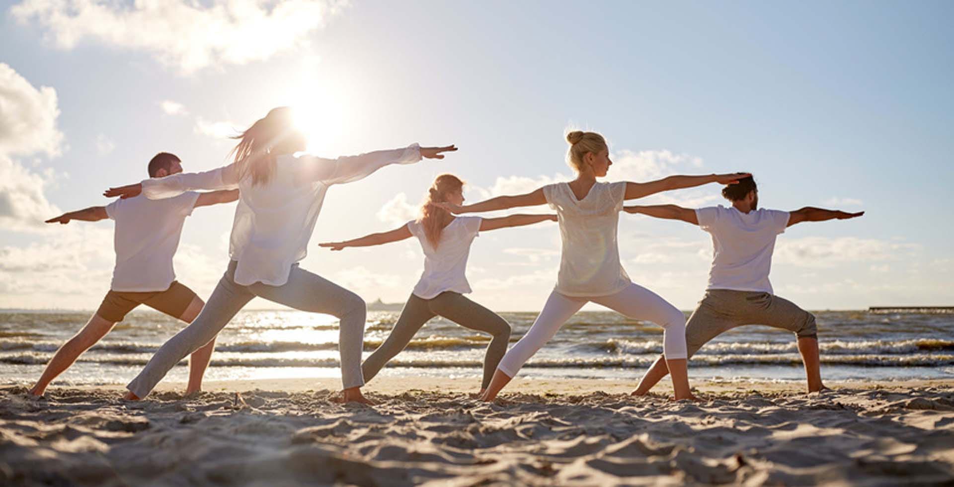 Yoga-Gruppe in Krieger-Position am Strand von Rügen bei Sonnenaufgang bei einem Yoga-Retreat vom Vju Hotel.