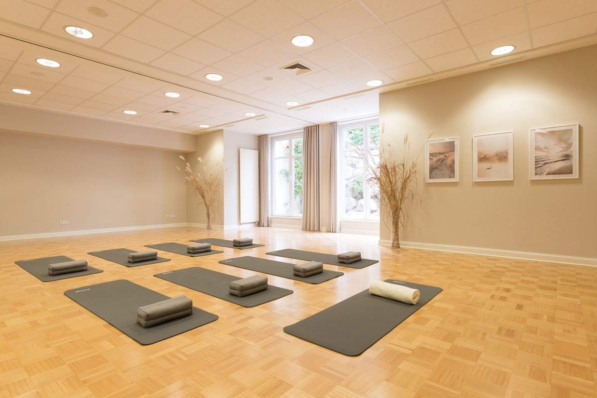 Heller Yogaraum mit Matten und Kissen auf Holzboden, stilvolle Einrichtung und warmes Tageslicht bei Ihrem Yoga-Retreat auf Rügen.