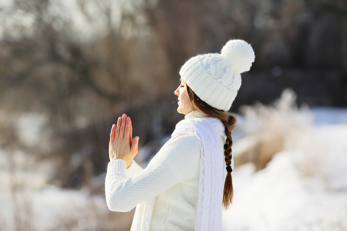 Frau in warmer Winterkleidung meditiert in verschneiter Natur, ruhige und friedliche Atmosphäre beim Yoga-Retreat im Vju Hotel.