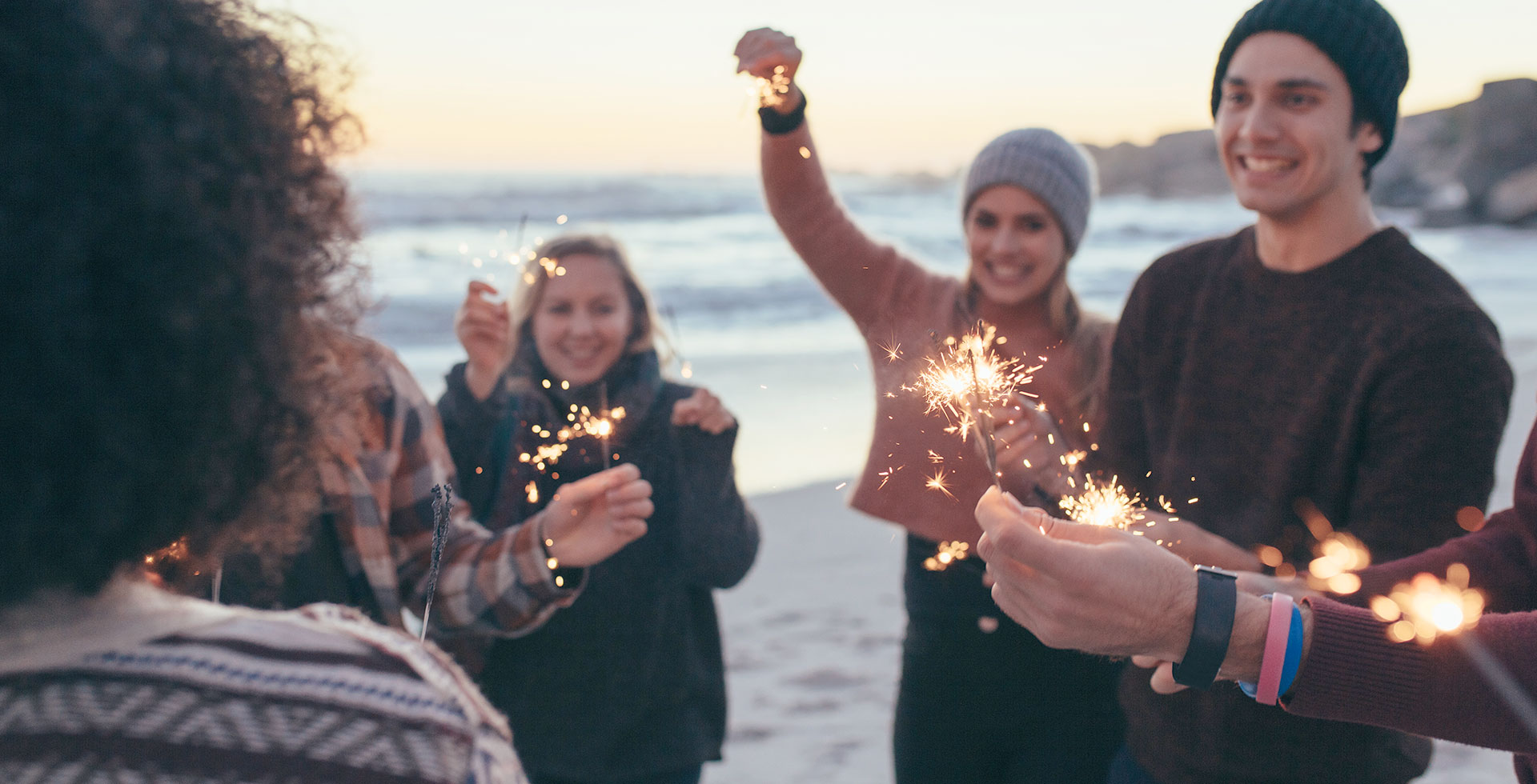 Gruppe von Menschen feiert mit Wunderkerzen am Strand des Wyn. Strandhotel auf Sylt bei Sonnenuntergang.