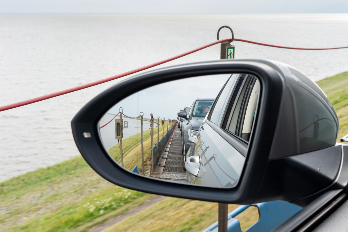 Autos auf einem Zug in Richtung Sylt zum Wyn. Strandhotel, gesehen im Rückspiegel eines Fahrzeugs, mit Meer im Hintergrund.