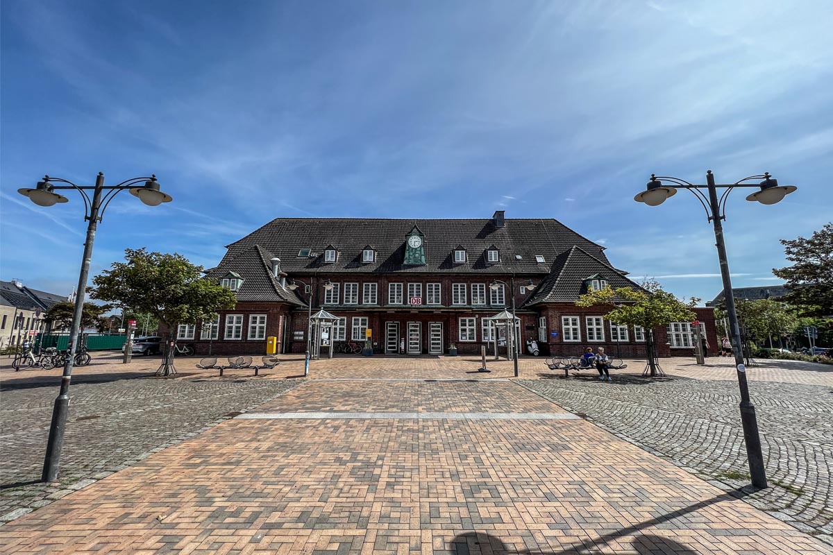 Der historische Bahnhof Westerland auf Sylt mit gepflastertem Vorplatz und Straßenlaternen bei klarem Himmel.