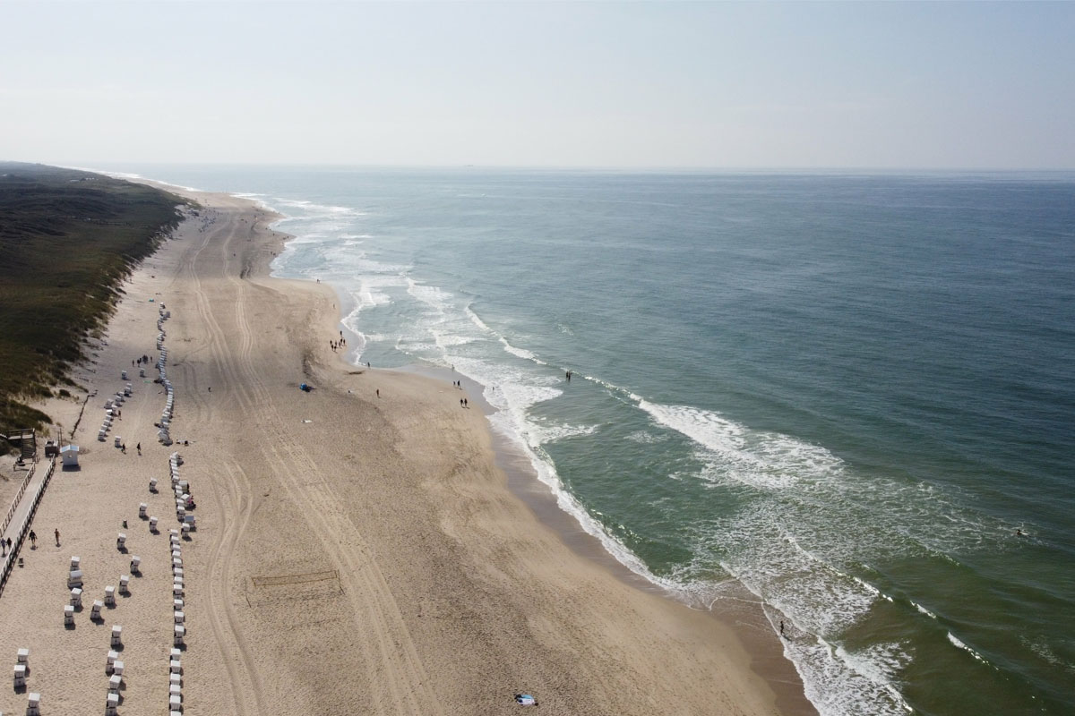 Luftaufnahme des weitläufigen Strandes von Sylt mit der Nordsee im Hintergrund zu sehen bei Anreise mit Flugzeug.
