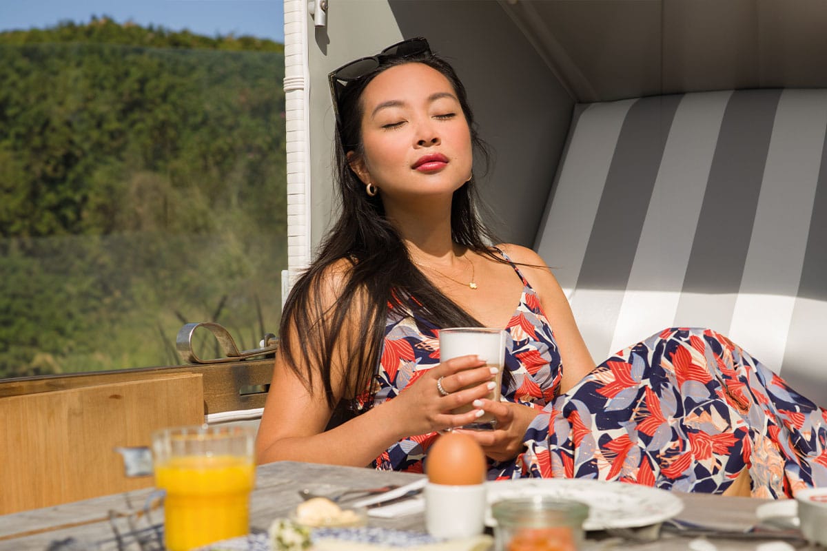 Frau entspannt beim Frühstück im Strandkorb des Wyn. Strandhotels im Urlaub auf Sylt mit frischem Saft und Kaffee.