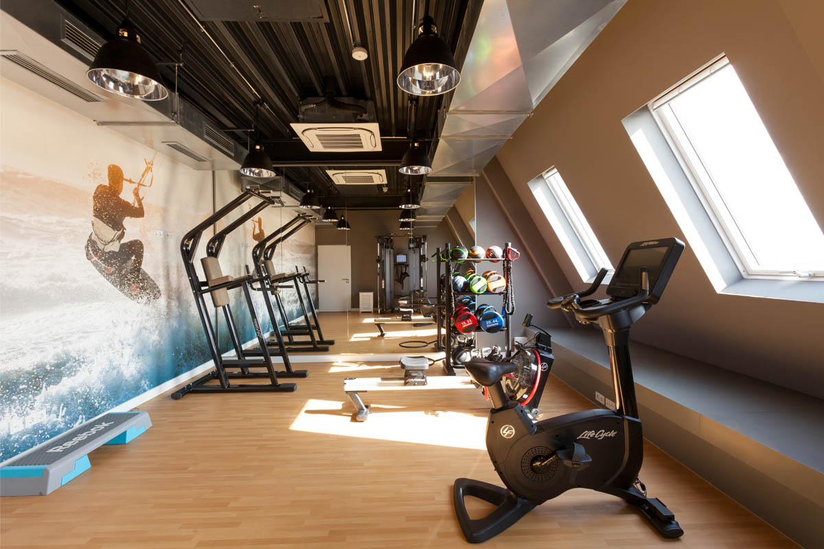 Moderner Fitnessraum für ein Workout im Wyn. Strandhotel auf Sylt mit Trainingsgeräten und Kitesurf-Wandmotiv